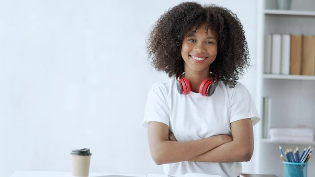 Young student smiling while posing with crossed arms in a modern office, wearing headphones and radiating happiness