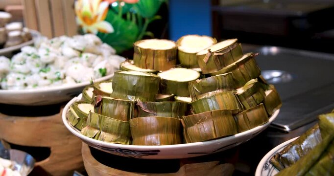 Cooked glutinous rice cake, Vietnamese new year food tet buffet Vietnam New Year rice cake in palm leaf with peas and meat slice on grey plate