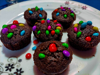 Muffin cakes on a plate are decorated with colorful gems chocolate