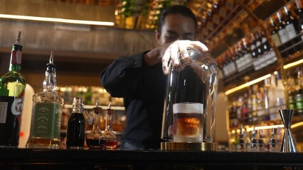 Asian bartender serving mist smoky classical mixing whiskey cocktail fantastic presentation, recommending special welcome tasty creative advertisement drink at beverage counter bar luxury. Vinosity.