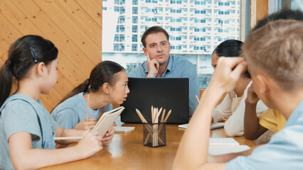 Caucasian teacher and smart boy discuss about project at classroom. Professional instructor talking about classwork while giving a paper to highschool child with diverse student listen. Edification.