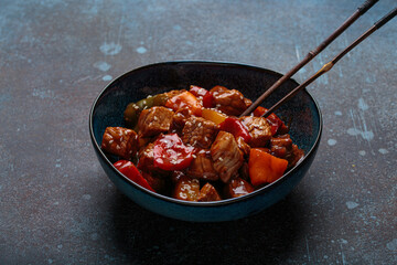 Delicious serving of sweet and sour pork is presented in a blue bowl, with chopsticks, Asian cuisine