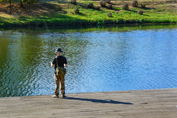 Back view of a man fishing alone at the river. A man with a fishing rod and in fishing gear in the...