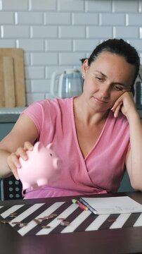 Vertical video. Young woman empties coins from a piggy bank onto a table, focusing on budgeting
