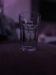 A transparent glass set on a dark surface, captured in low light. The subtle purple hues and reflections create a moody, contemplative atmosphere.