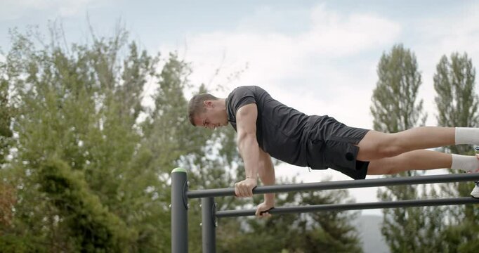 A young athletic man works out on parallel bars in the park, doing dips as part of his fitness and exercise routine, promoting health and strength.