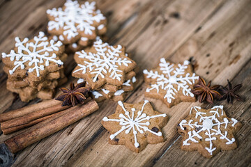 Gingerbread cookies with white snowflake icing, arranged with cinnamon sticks and star anise on a rustic wooden background, creating a festive and cozy holiday atmosphere.