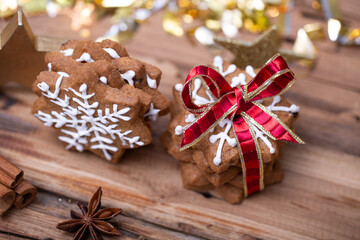 Stacks of gingerbread star cookies decorated with white icing, one tied with a red ribbon, on a wooden table with festive decorations and warm bokeh lights in the background.