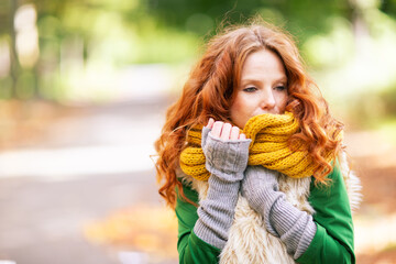 Woman with red hair, wearing gray fingerless gloves, sips herbal tea from a glass cup while looking...