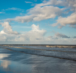 Obraz premium A beautiful lonely sea beach with blue sky and scattered clouds reflect on the sea water at the dusk.