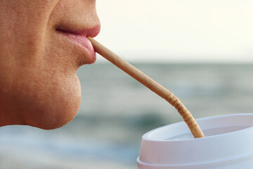 A person sipping a beverage using a recyclable paper straw.