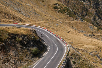 A lone cyclist rides along a winding mountain road, showcasing the rugged beauty of the landscape. 