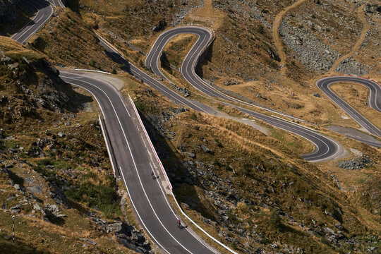 Aerial view of a winding mountain road with cyclists. Road is surrounded by dry grass and rocky terrain. Sportsmen training hard on bicycle outdoors.Sports motivation. Cycling professional group ride.