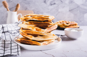 Stack of freshly baked Belgian waffles on plate and sour cream in bowl on table