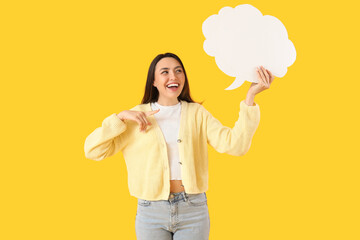 Young woman pointing at blank speech bubble on yellow background