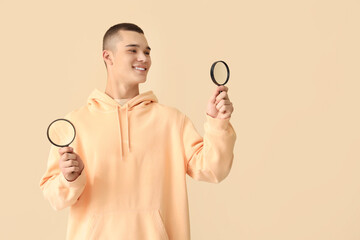 Young man with magnifiers on beige background