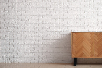 Stylish wooden chest of drawers near light brick wall