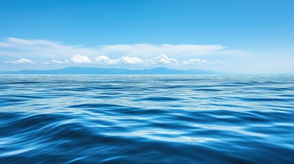 Obraz premium A tranquil blue ocean stretches out to the horizon, with a distant mountain range visible in the background under a clear sky.