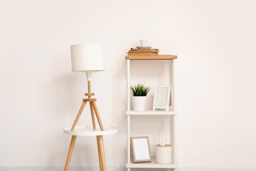 Lamp on small table and shelving unit with decor near white wall