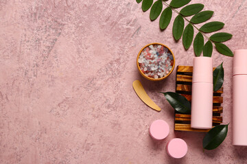 Bottles and jars of cosmetic products with sea salt on pink background