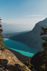 high point of view of a turquoise water lake next to a tall rocky mountain in summer with bad air...