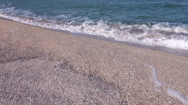 Mother-of-pearl sea surf. A quiet sea, sandy-shell beach, colors the crest of the rolling waves