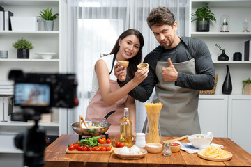 Couple chef influencers on cooking show presenting ingredient of spaghetti, meat, chilli, tomato, garlic and seasoning sauce's homemade special recipe recording on camera on live channel. Postulate.