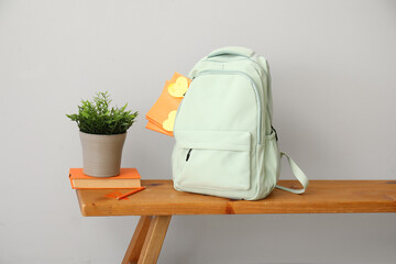 School backpack with stationery and houseplant on wooden table near light wall