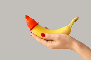 Woman holding banana with condom on light background. Sex concept