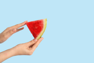 Female hands with slice of ripe watermelon on blue background