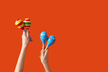 Female hands holding maracas on orange background
