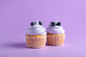 Tasty cupcakes with blueberries on lilac background