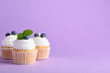 Tasty cupcakes with blueberries on lilac background