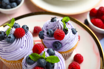 Plate of delicious cupcakes with blueberries, raspberries and mint on table