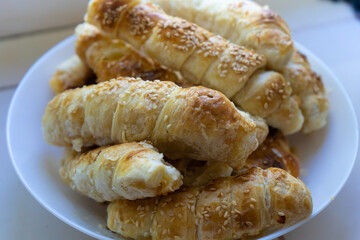 Baked puff pastry homemade rolls with sesame on white plate as a snack for breakfast. Home meal close up