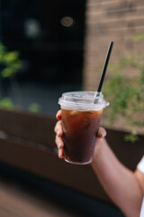 Closeup vertical cropped shot of unrecognizable woman holding takeaway plastic cup with iced beverage outdoors. Cup of cold bubble tea with straw in female hand. Concept of drink, lifestyle, city life