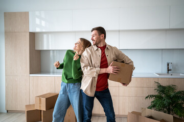 Happy couple enjoy on moving day playful dancing with cardboard boxes, smiling in new kitchen....