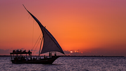 Voilier touristique naviguant devant le coucher de soleil avec le soleil se cachant derrière les nuages, Zanzibar, Tanzanie