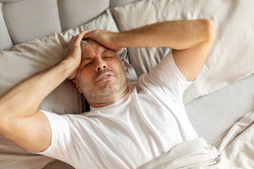 Sick European middle aged man lying in bed and touching head, tired male wake up with headache in...