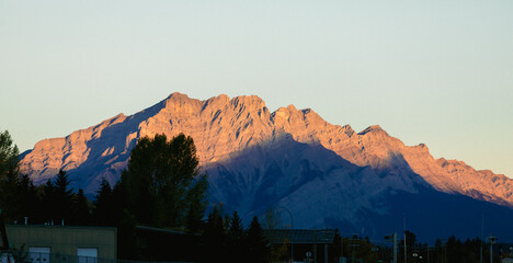 Golden sunset light illuminates the rugged peaks of a mountain range over a cloudless sky, creating a breathtaking natural scene.