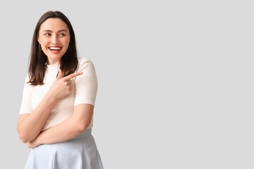 Smiling young woman pointing at something on grey background