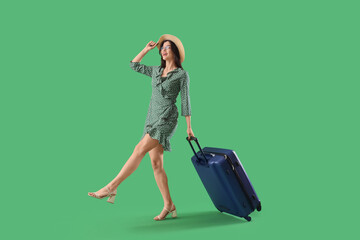Beautiful young happy female tourist with suitcase on green background