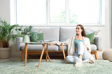 Young woman sitting on green carpet near grey sofa in living room