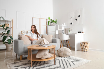 Young woman sitting on grey sofa in light living room