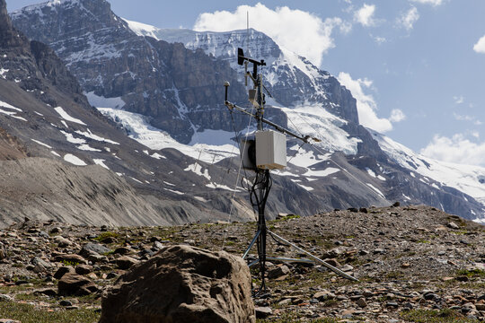 A detailed view of a weather monitoring station set against a backdrop of towering, snow-capped mountains, perfect for environmental data collection and scientific research photography. - Powered by Adobe