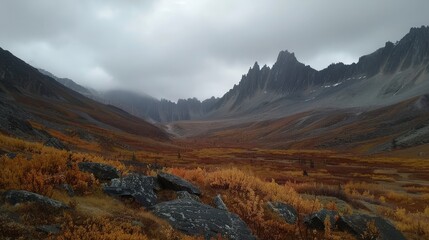 Obraz premium A misty, moody mountain valley with a dramatic, rocky backdrop. The fall foliage adds a splash of color to the rugged landscape.