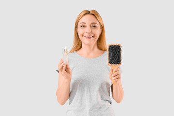 Mature woman with brush and serum for hair growth on light background