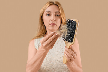Mature woman with hair loss problem and brush on beige background