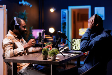Young interviewer adjusting the sound mixer while talking with guest, recording a talk show. Two african american men using podcast equipment, discussing different topics for their online audience.