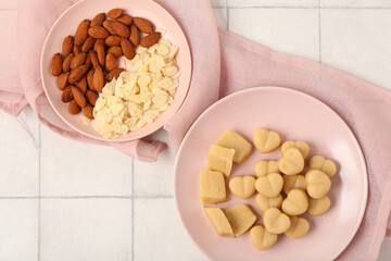 Plates with tasty marzipan candies, almond flakes and nuts on light tile table